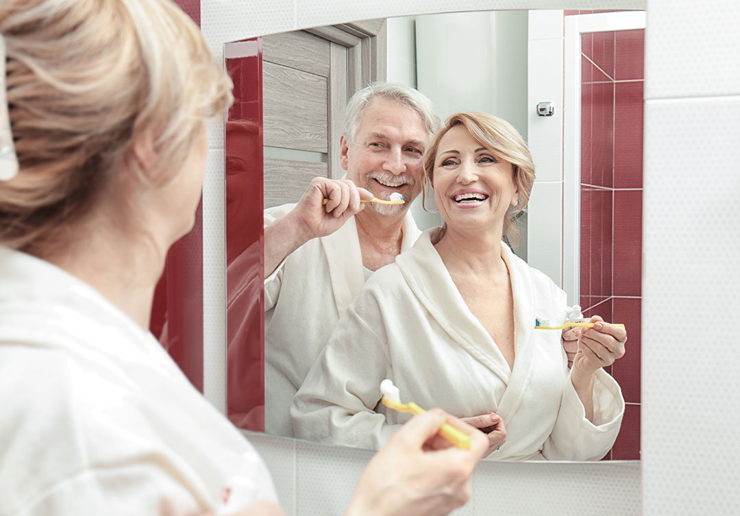 Senior Couple Smiles Brushing Teeth Mirror